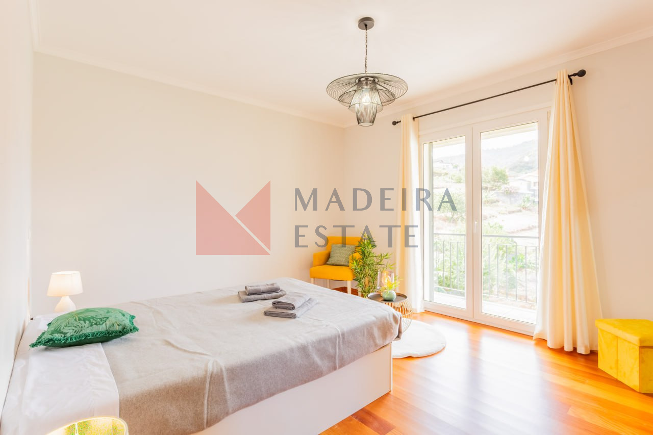 Bright master bedroom with panoramic windows, double bed, armchair, and ottoman in vacation rental home in Madeira