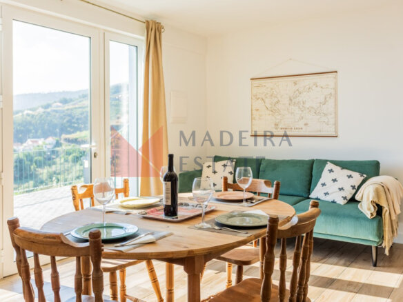 Cozy, bright living room with table, chairs, sofa, large window, and terrace access at Cantinho do Barreiro in Calheta, Madeira.
