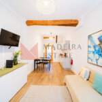 Гостиная открытой планировки с телевизором, диваном, комодом, предметами искусства и кухней в квартире для краткосрочной аренды в Фуншале