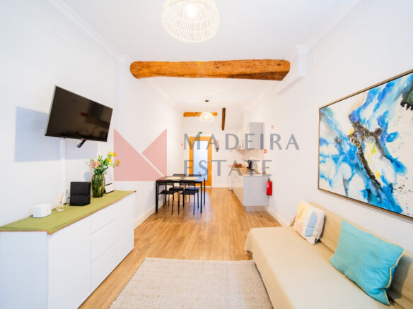 Open-plan living room with TV, sofa, dresser, artwork, and kitchen in a short-term rental apartment in Funchal