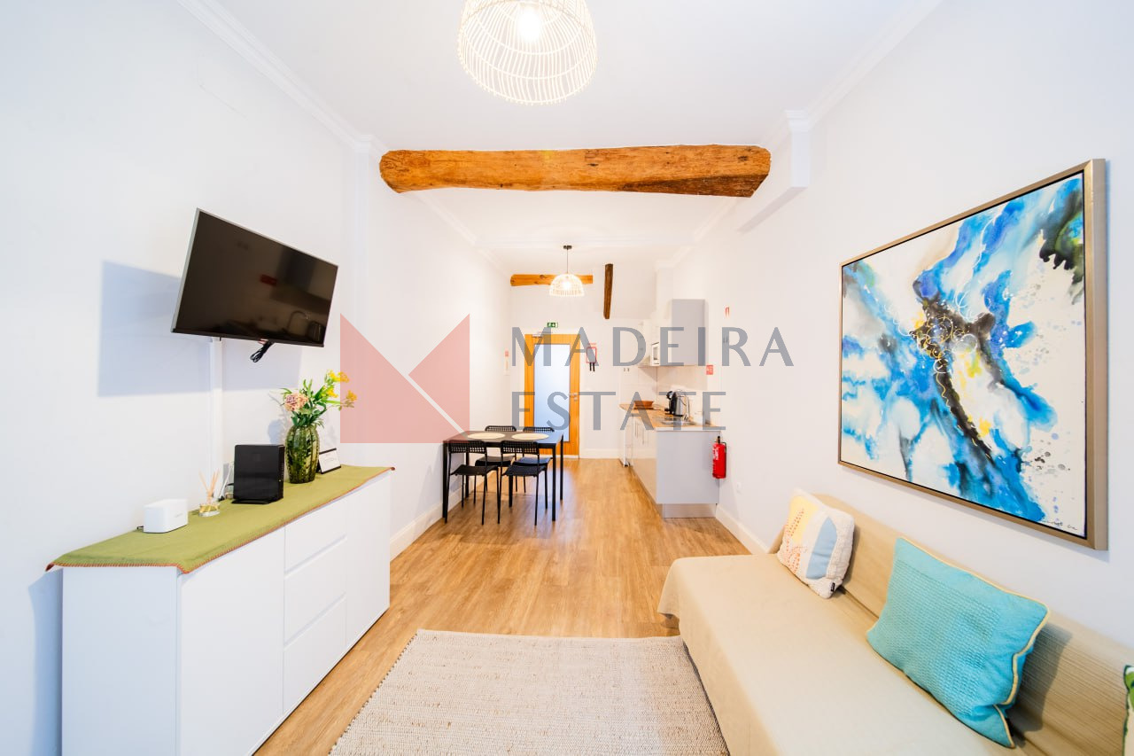 Sala de estar em plano aberto com televisão, sofá, cómoda, obras de arte e cozinha num apartamento de aluguer de curta duração no Funchal