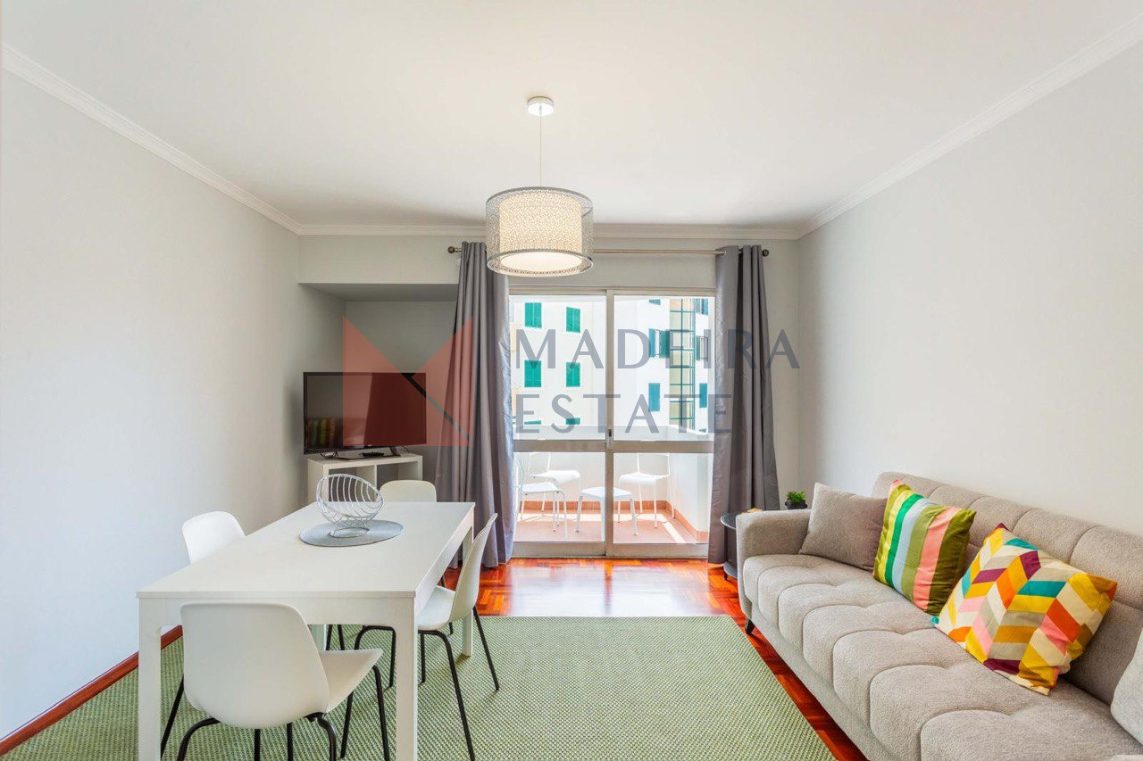Living Room with Balcony – JMF Apartment, Funchal, Madeira Bright living room with parquet floor, sofa, dining table, TV, and balcony access – JMF Apartment, Madeira short-term rental